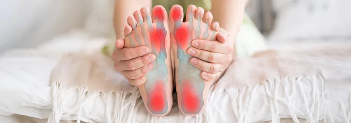 A person holding their feet while sitting on a bed,